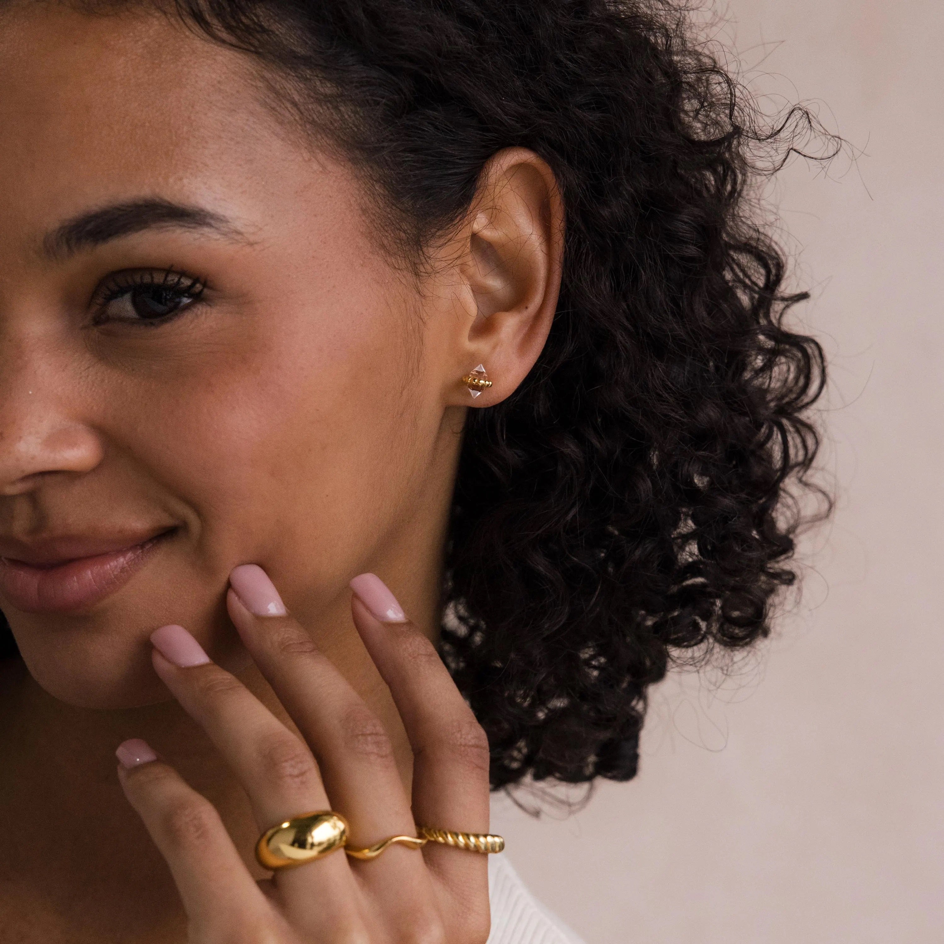 Smiling woman with curly hair wears luminous Beaded Herkimer Studs, touching her face with manicured fingers.