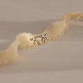 A pair of silver bow stud earrings placed on an ivory frayed-edge fabric.