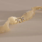 A pair of silver bow stud earrings placed on an ivory frayed-edge fabric.