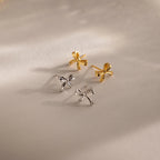 Product flat lay featuring two pairs of bow stud earrings—one gold and one white gold—arranged under soft lighting on a neutral background.