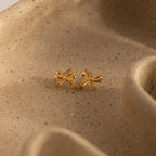 Gold bow stud earrings resting on a bed of sand, accentuating their warm tone and soft, graceful curves.