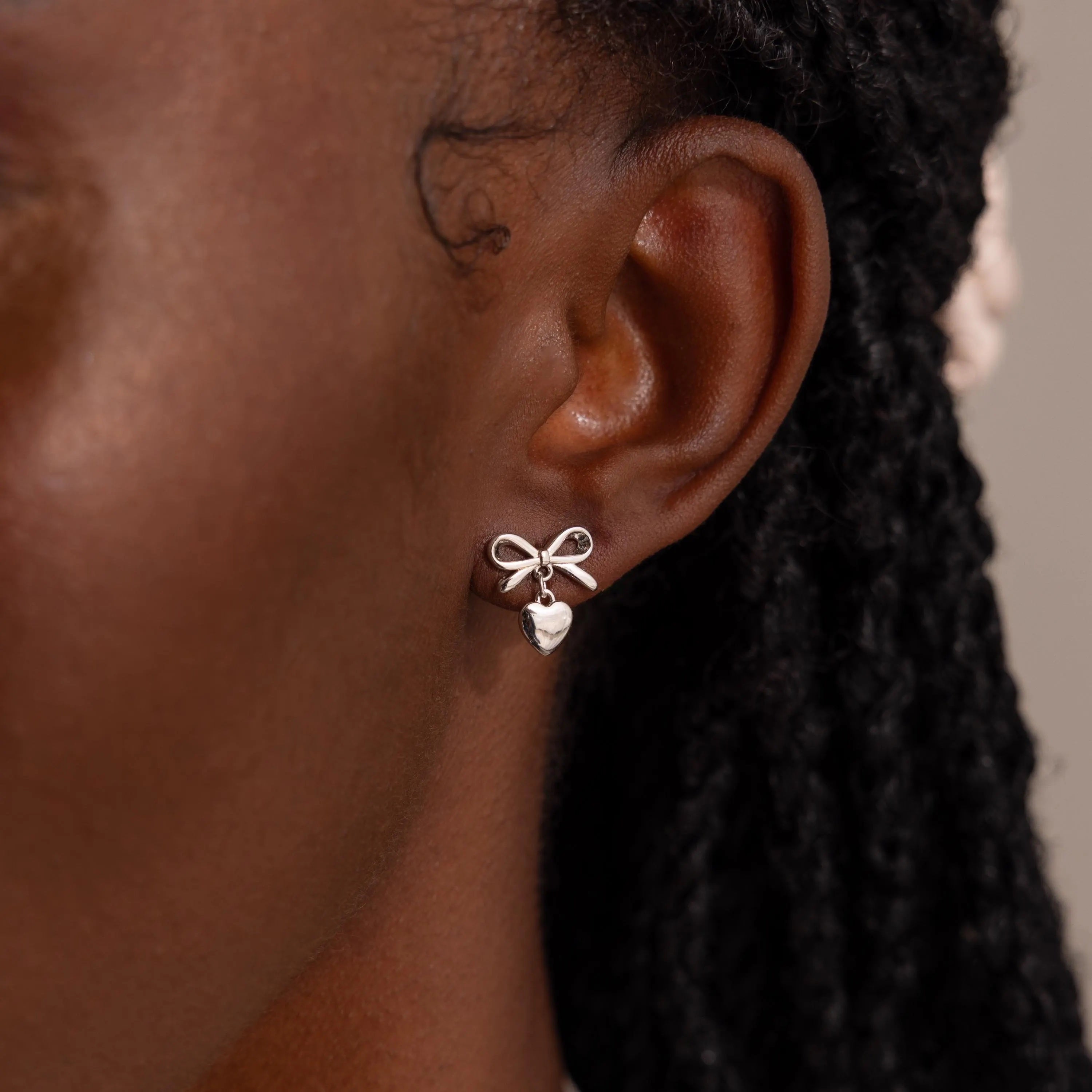 Close-up of a woman wearing a silver version of the bow heart stud earring, which sits elegantly against her earlobe.
