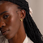 A woman wearing the gold bow heart stud earring paired with a small gold heart cartilage stud and a hoop earring.