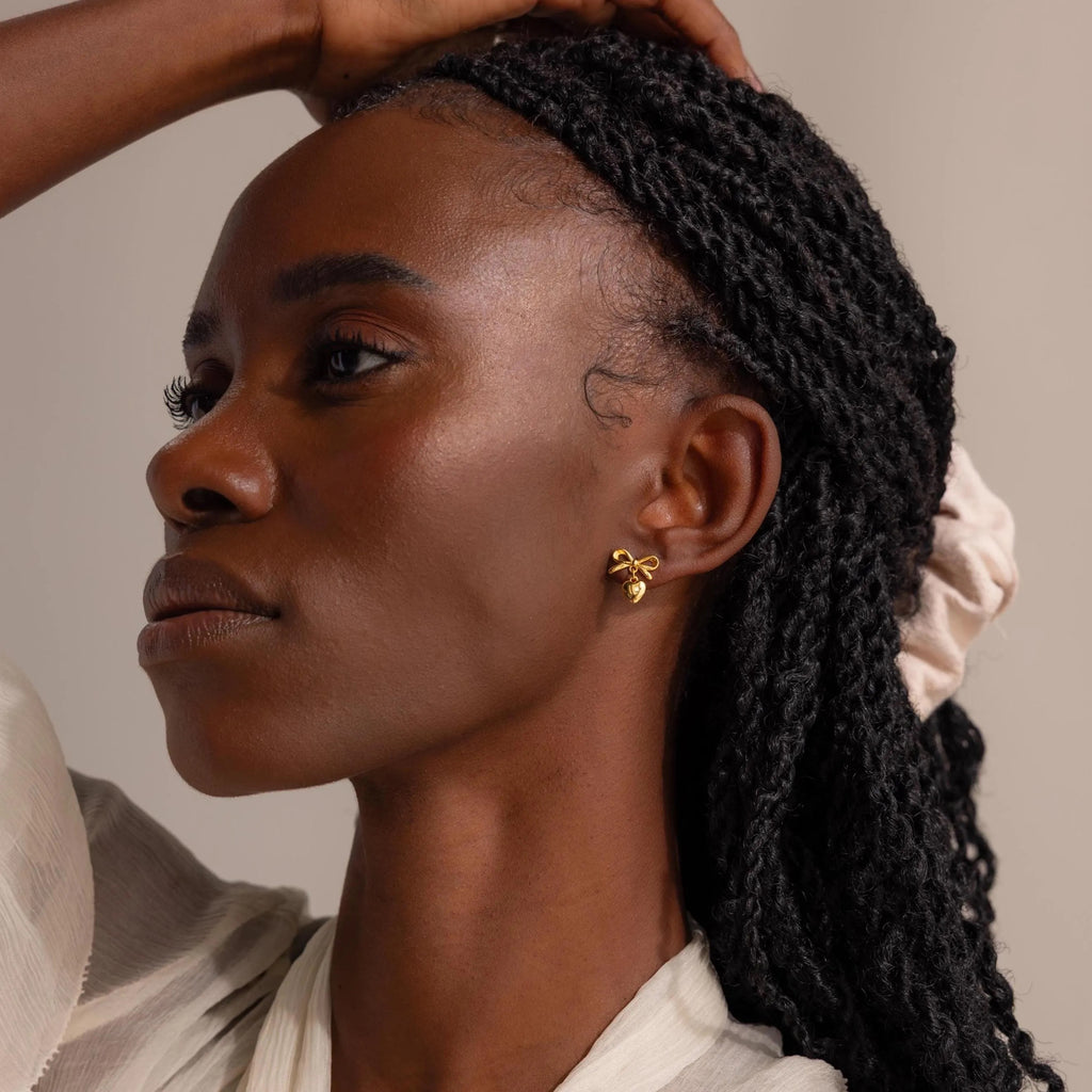 Model showcasing the gold bow and heart dangle drop stud earring.