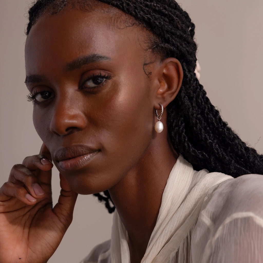 Front-facing portrait of a woman wearing the Twisted Pearl Hoop Earring in silver