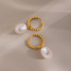 Two gold twisted hoop earrings with pearls shown flat on a beige surface, one positioned upright and the other tilted for depth.