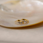 Lace Diamond Huggies—gold hoop earrings adorned with small clear gemstones—are elegantly displayed on a glossy, light-colored dish.