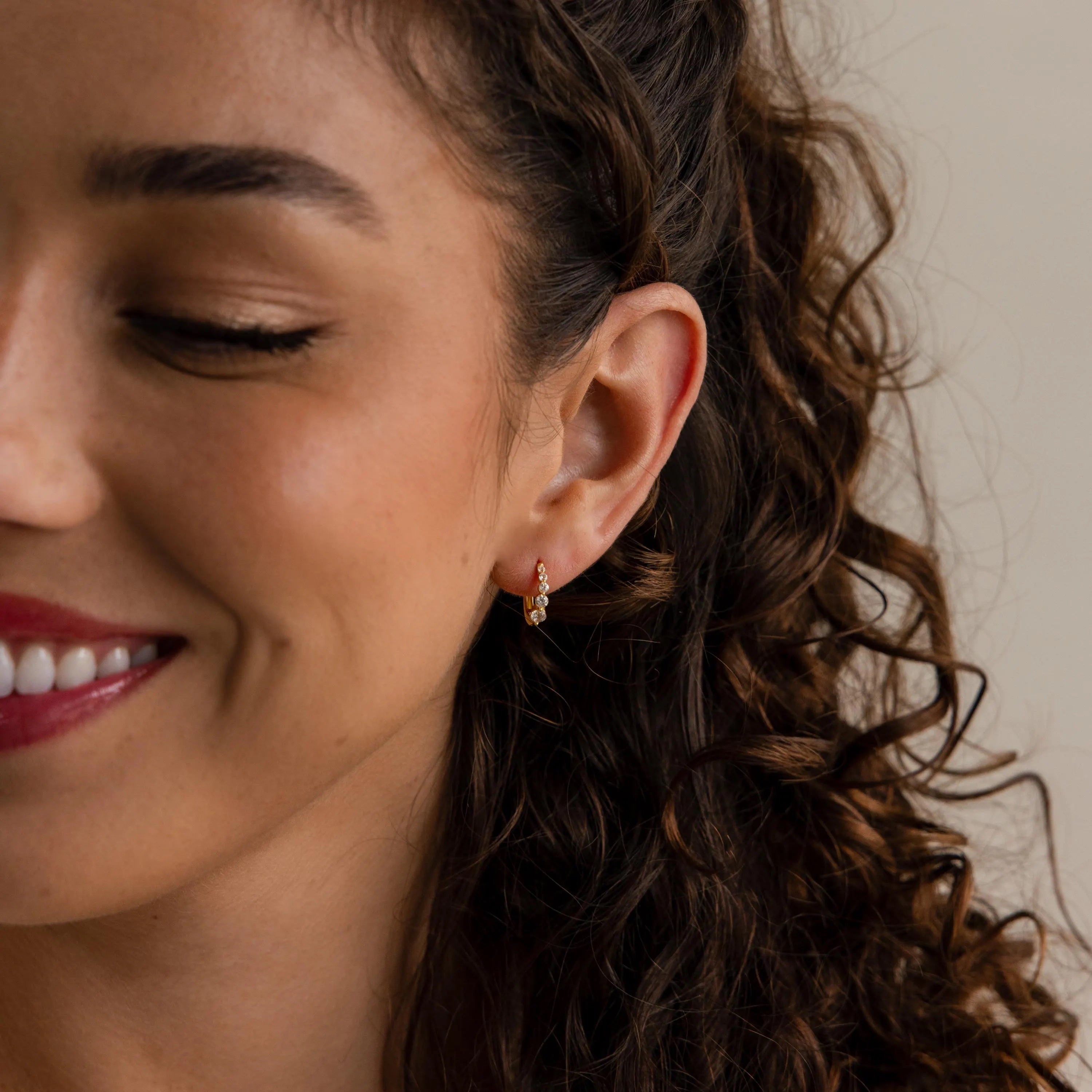A smiling woman with curly hair wears Lace Diamond Huggies in an elegant close-up side profile.