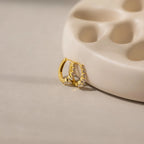 The Lace Diamond Huggies, elegant earrings with embedded crystals, rest against a beige curved ceramic dish, echoing the timeless style of classic diamond hoops.