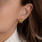 Close-up of a woman's ear wearing the Triple Loop Huggie Earrings in gold, styled with brown hair and a white knit sweater—an ideal accessory for everyday wear.
