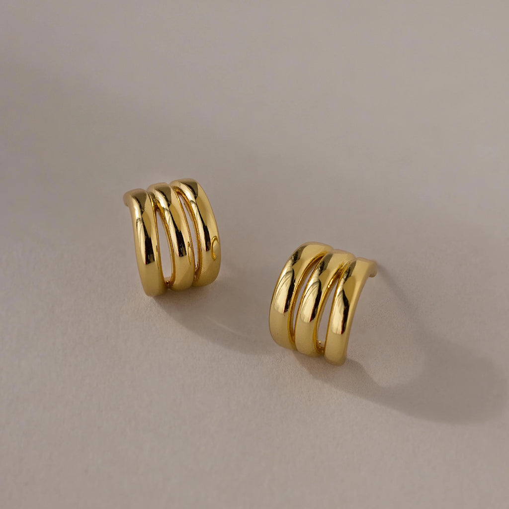 Triple Loop Huggie Earrings with a gold triple-band design, ideal for everyday wear or stacking, shown on a neutral background.