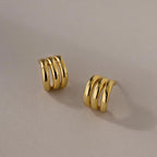 Triple Loop Huggie Earrings with a gold triple-band design, ideal for everyday wear or stacking, shown on a neutral background.