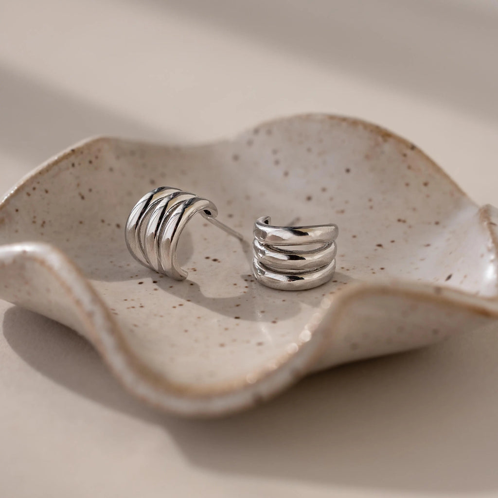 Triple Loop Huggie Earrings rest on a wavy, speckled ceramic dish in soft natural light—ideal for stacked ear styling or effortless everyday wear.