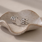 Triple Loop Huggie Earrings rest on a wavy, speckled ceramic dish in soft natural light—ideal for stacked ear styling or effortless everyday wear.