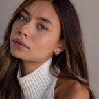 Woman with long brown hair wears a white sleeveless turtleneck and gold Triple Loop Huggie Earrings, creating a stylish stacked ear look ideal for everyday wear.