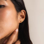 Close-up of a woman’s ear wearing one gold Twisted Snake Earring. She is gently touching her jawline with her index finger