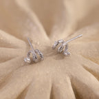 Pair of silver Twisted Snake Earrings displayed on a sandy-textured surface