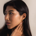 Model showing an ear styling with multiple piercings. The gold Twisted Snake Earring is worn on the lower lobe, paired with other minimal snake earrings  along the cartilage and upper ear, demonstrating a curated ear look
