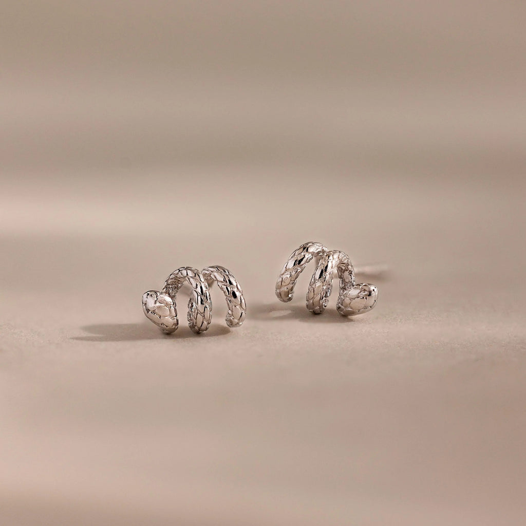 Silver 3D twisted snake stud earrings resting on a neutral surface.