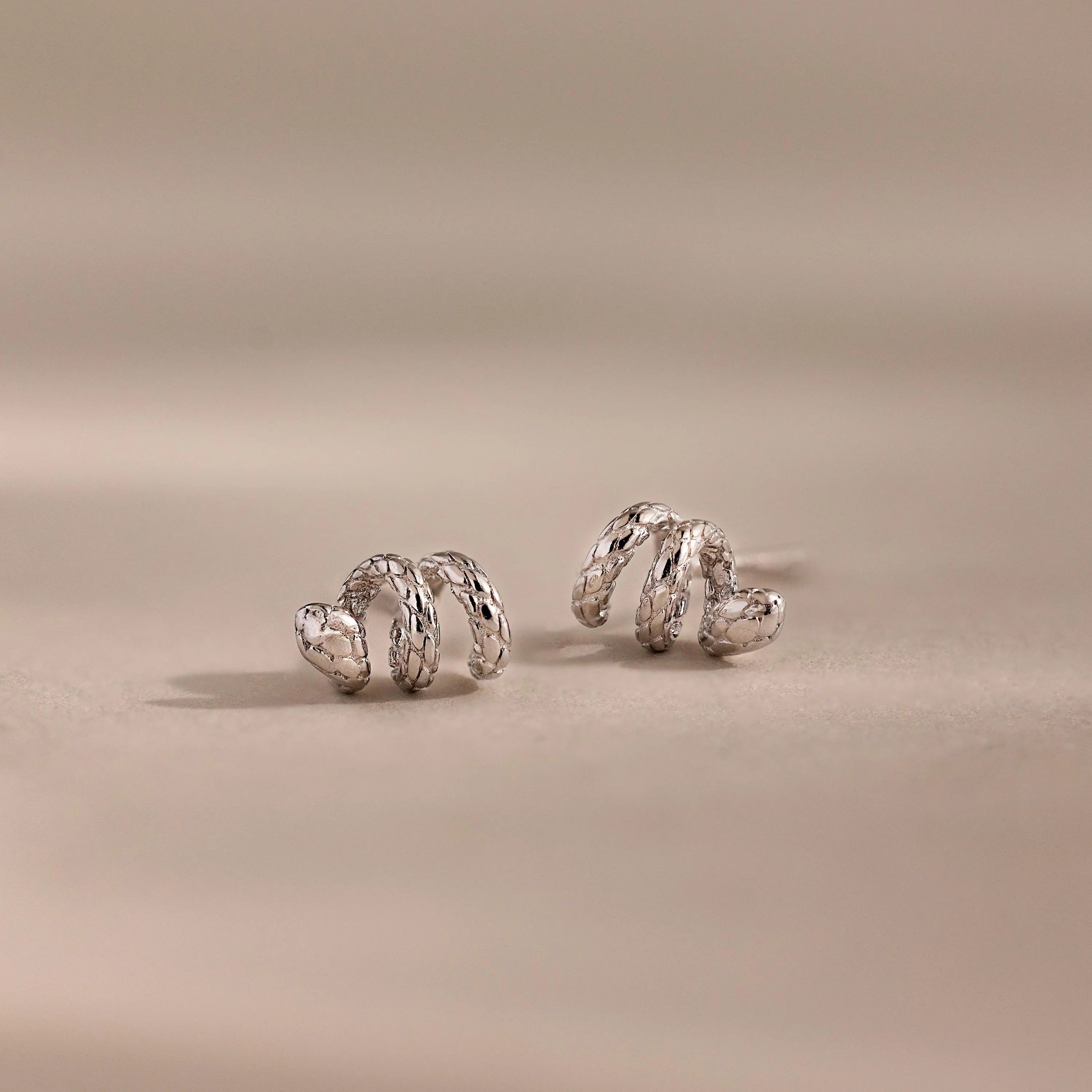 Silver 3D twisted snake stud earrings resting on a neutral surface.
