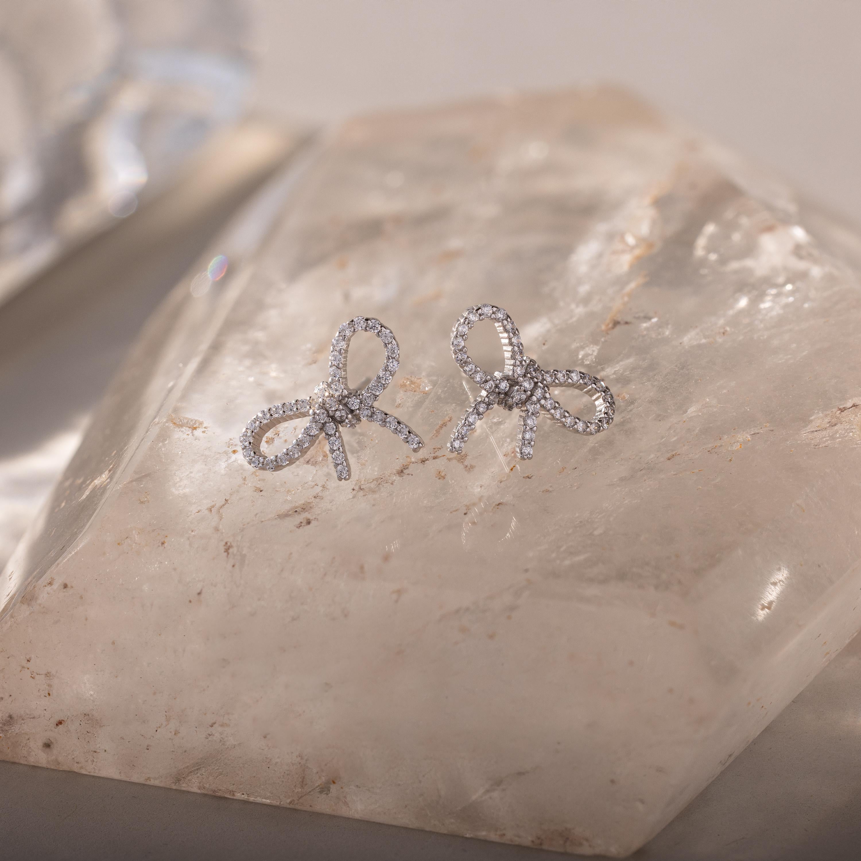 Silver pavé bow stud earrings displayed on a clear quartz crystal, sparkling under soft natural light.