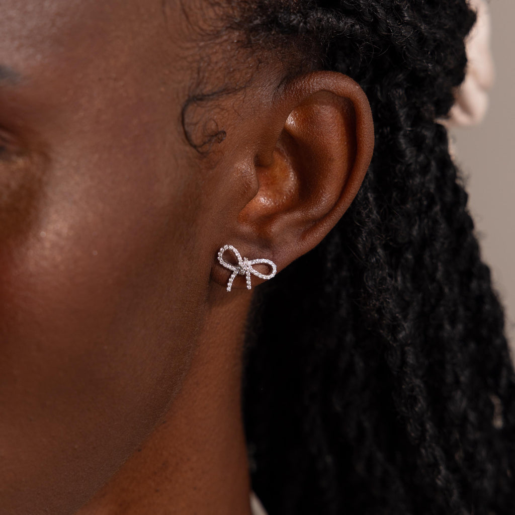 Close-up of model wearing a silver pavé bow stud earring, showcasing its sparkling detail and dainty, feminine silhouette.