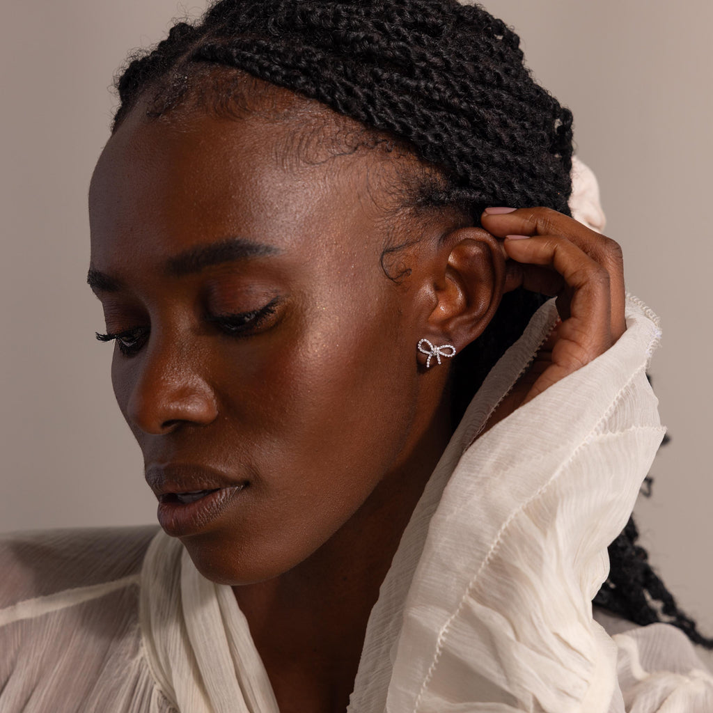 Model wearing sparkling silver pavé bow stud earrings, styled with a soft ivory blouse, highlighting the delicate, feminine design.