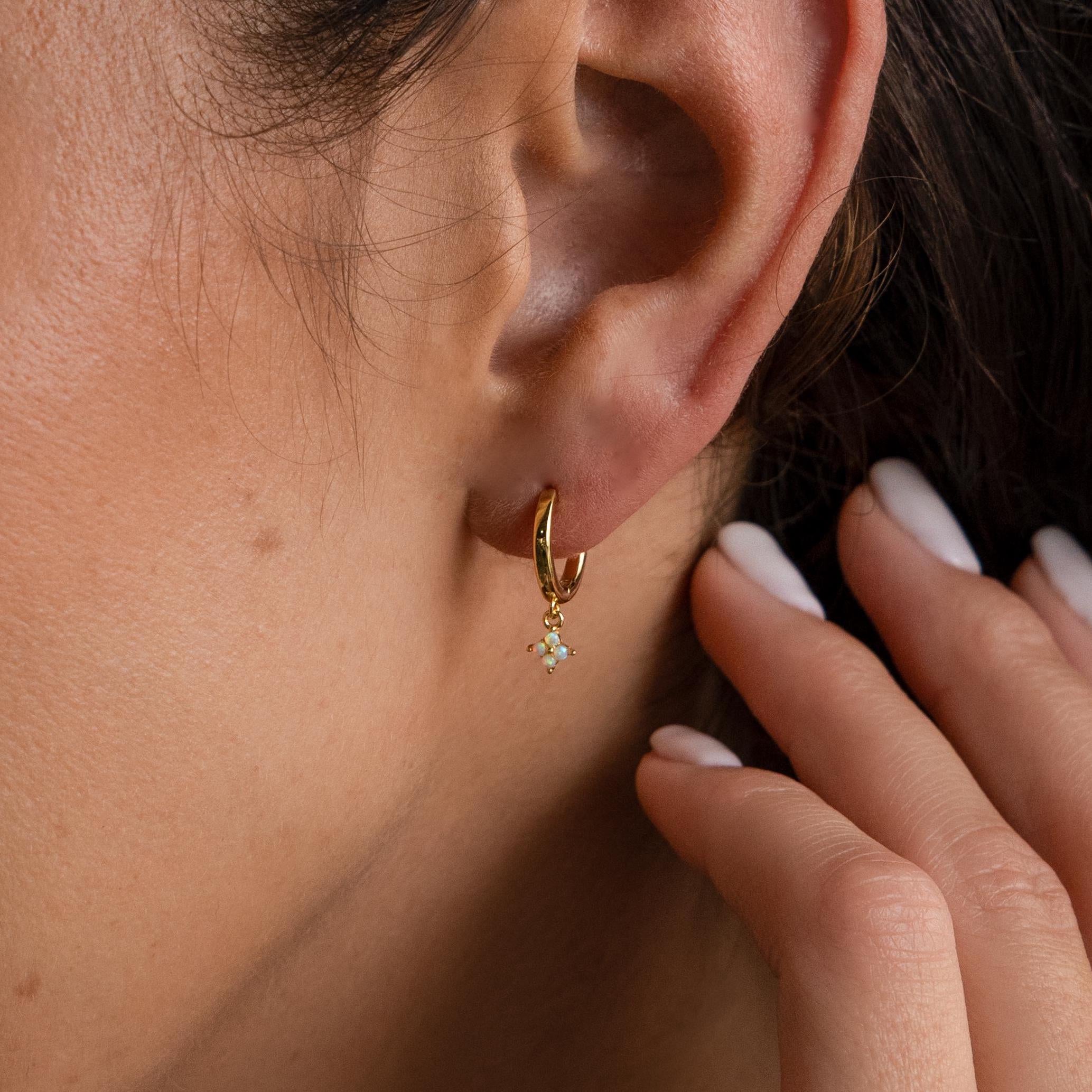 A close-up of an ear wearing Ivy Birthstone Hoops—small gold earrings with a delicate dangling gemstone, hand near the ear—ideal for those who love personalized jewelry.