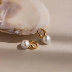 The Dome Pearl Huggies rest beside an open seashell on a soft beige background.