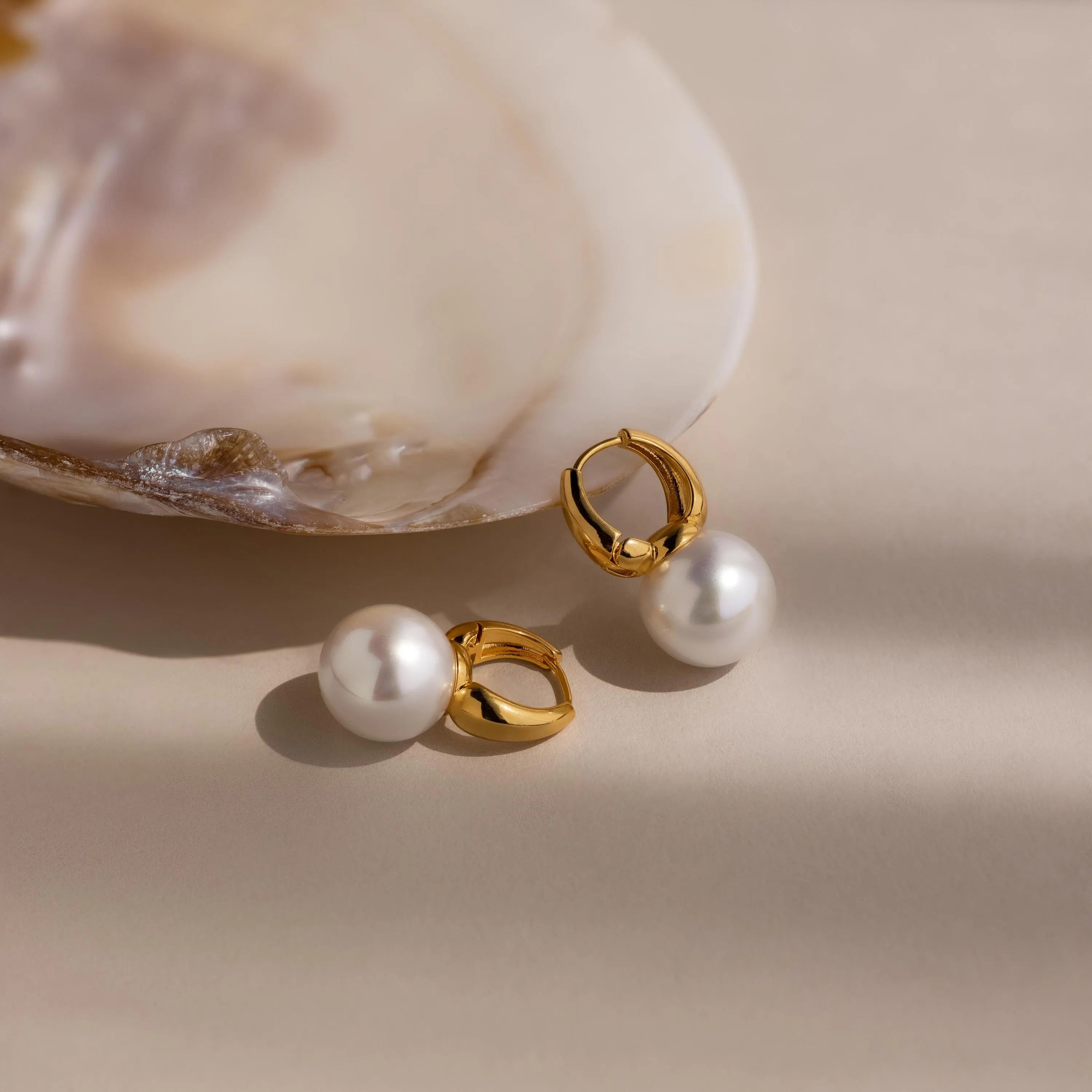 The Dome Pearl Huggies rest beside an open seashell on a soft beige background.