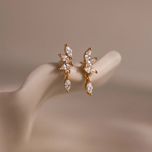 Close-up of dainty gold CZ diamond drop earrings with four marquise-cut stones, displayed on a neutral surface.
