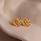 Close-up of a pair of gold Ribbed Heart Initial Studs with the letter R in CZ pave detailing, resting against a neutral background.