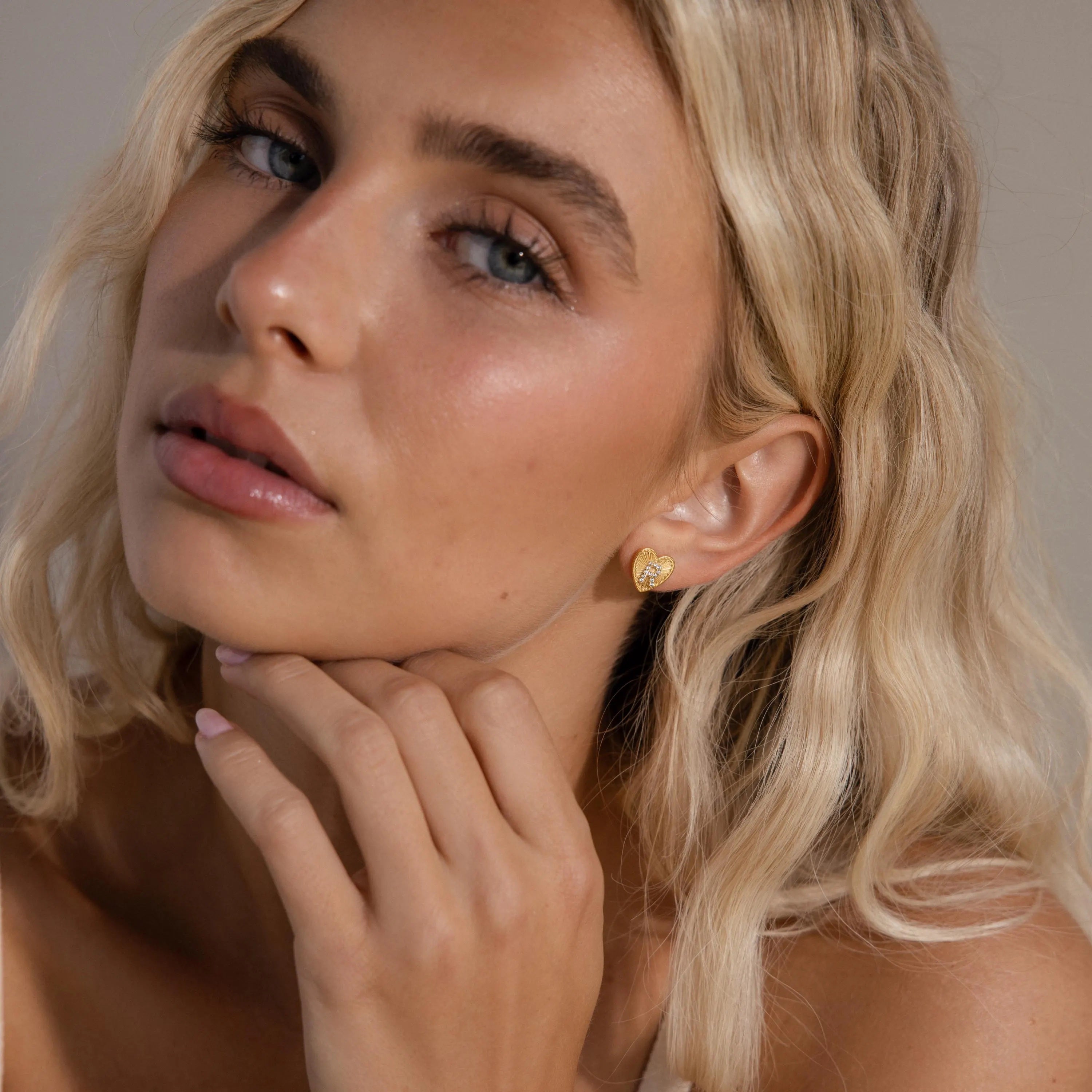 Model wearing a gold Ribbed Heart Initial Stud Earring with the letter R in CZ pave detailing.