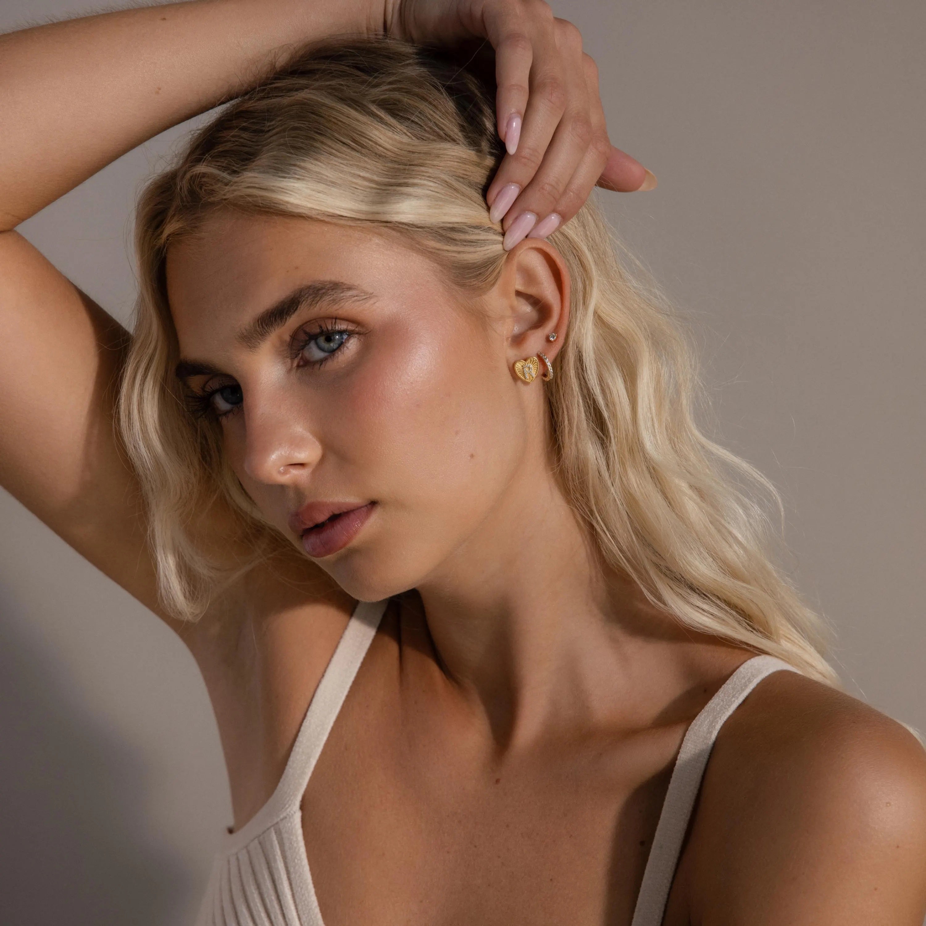 Far-view of model wearing a gold Ribbed Heart Initial Earring with a pave letter R, stacked with a pave huggie hoop and dainty diamond stud.