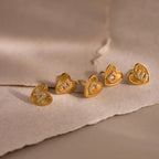 5 gold Ribbed Heart Initial Stud Earrings with sparkling A, B, C, D, and E pave letters displayed on textured neutral paper backdrop.