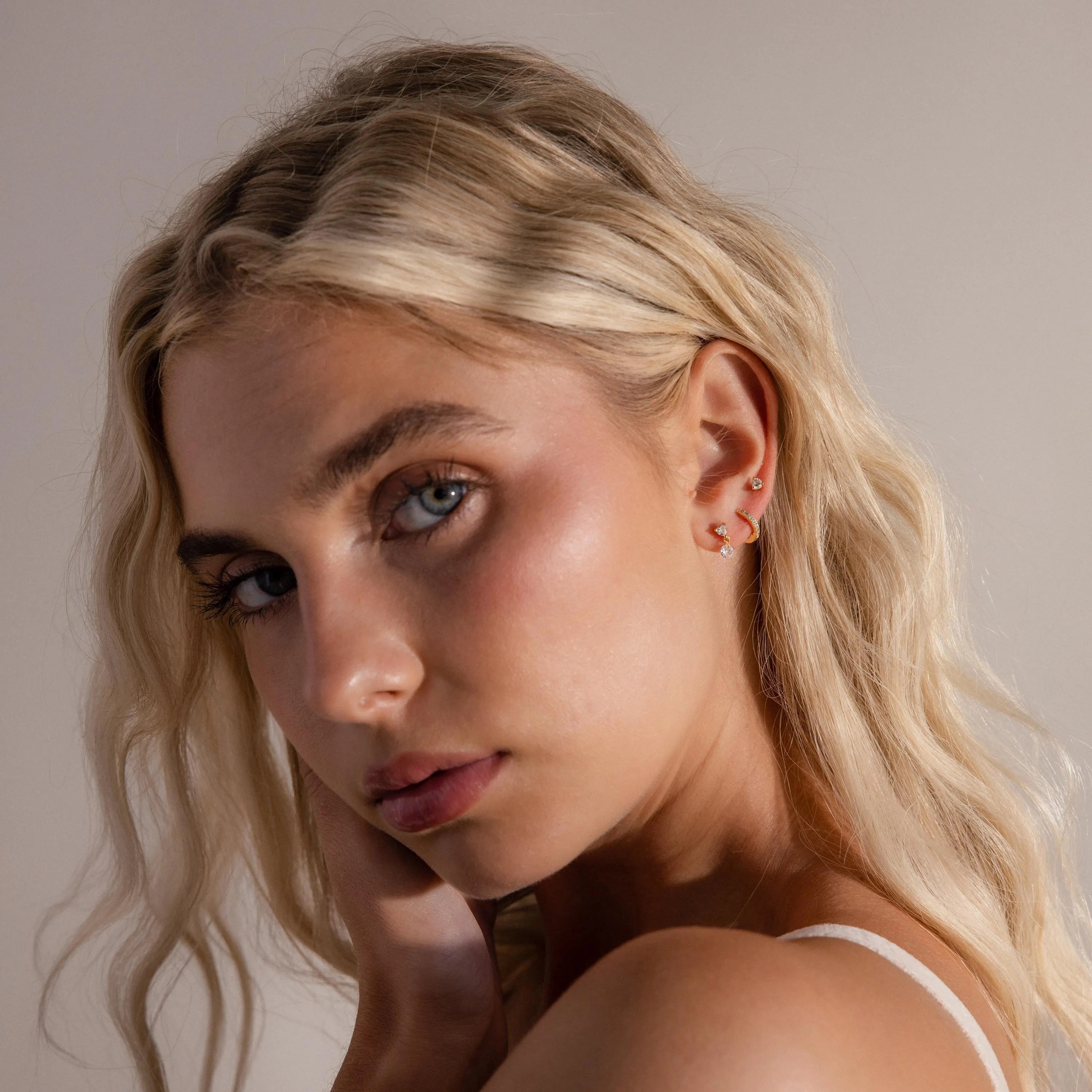 Model wearing gold Heart Drop Flat Back earrings alongside a pave diamond huggie and a single diamond stud, showcasing a stacked look
