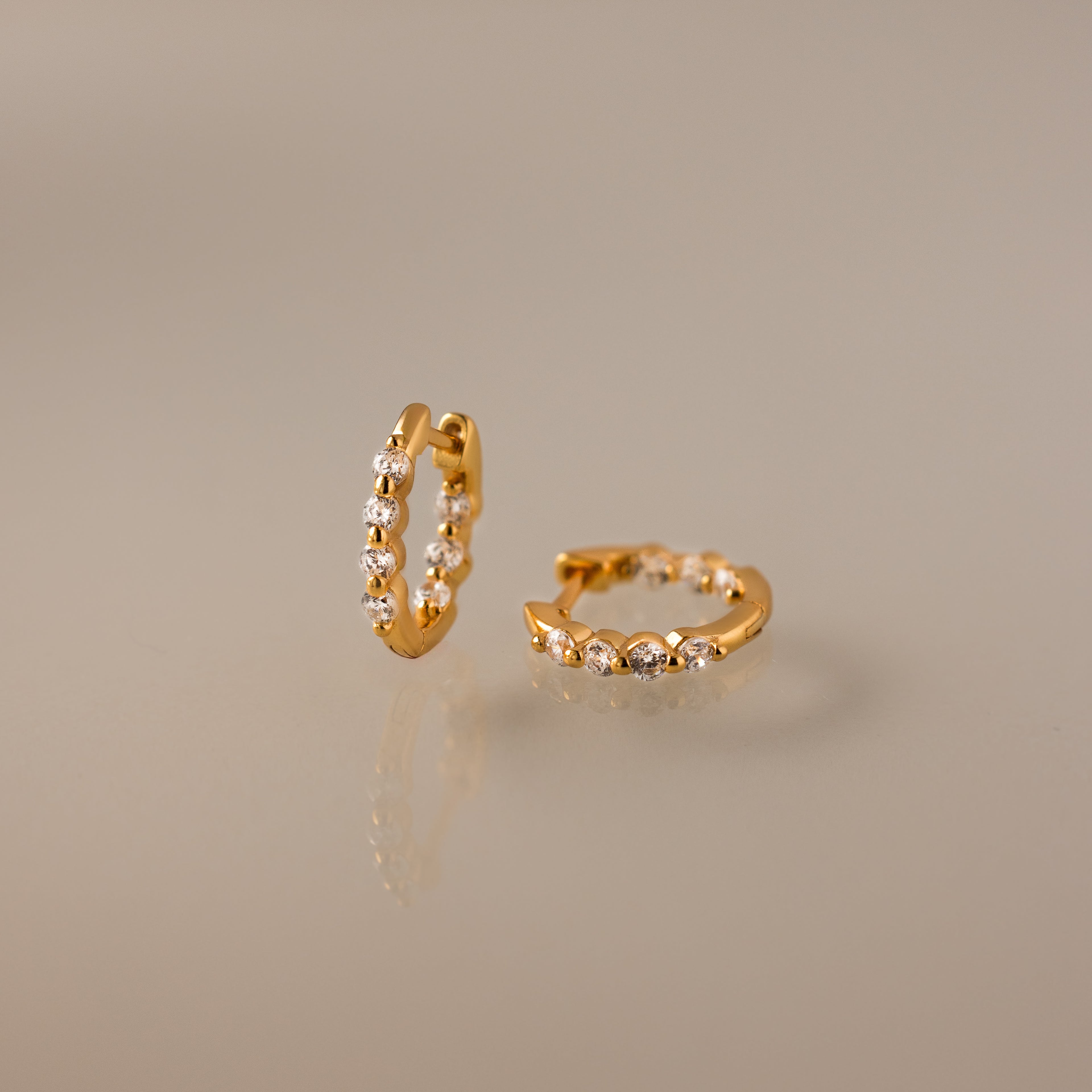 A pair of Mini Diamond Beaded Huggies, small gold modern earrings with a row of clear gemstones, displayed on a neutral background.