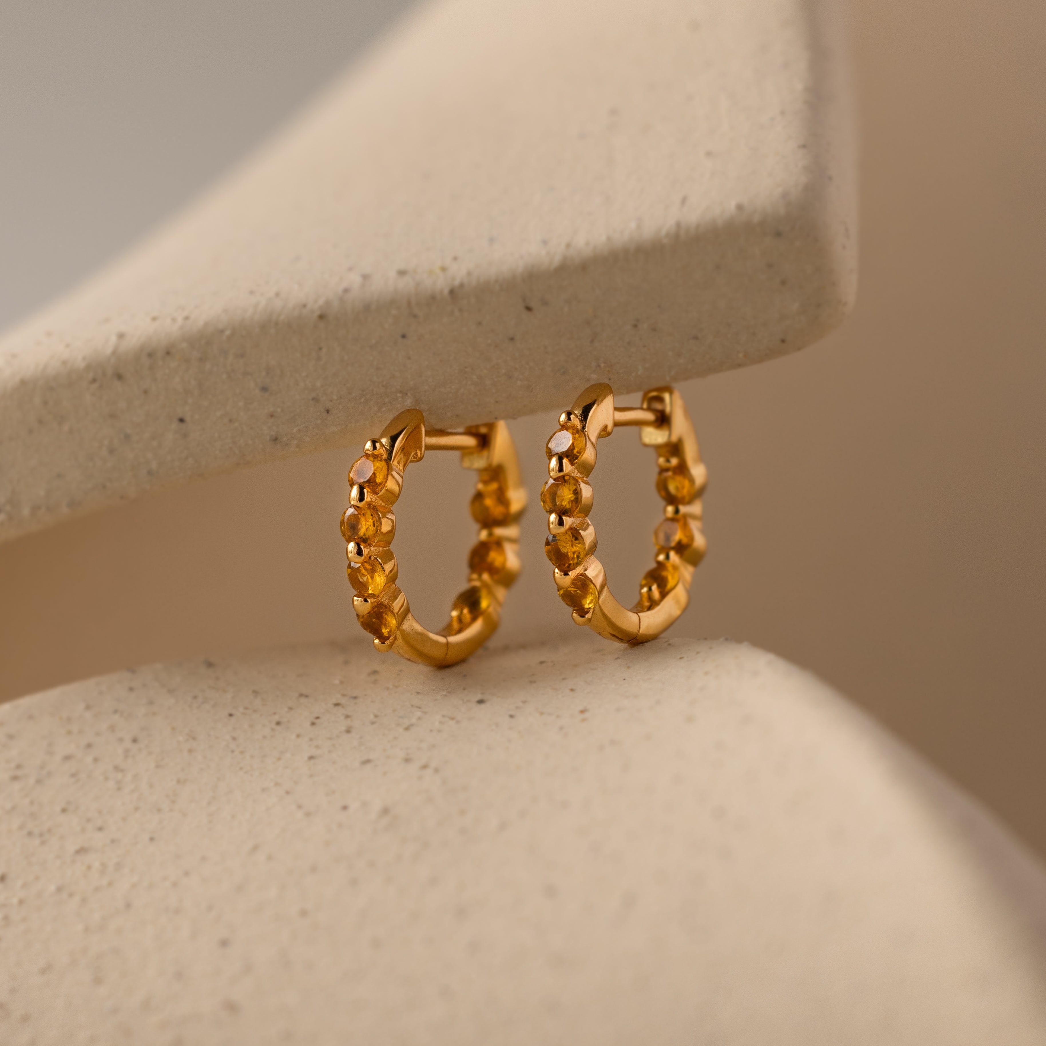 Mini Birthstone Beaded Huggies with a textured design shine against a soft beige background—add a unique touch of birthstone jewelry elegance to your look.