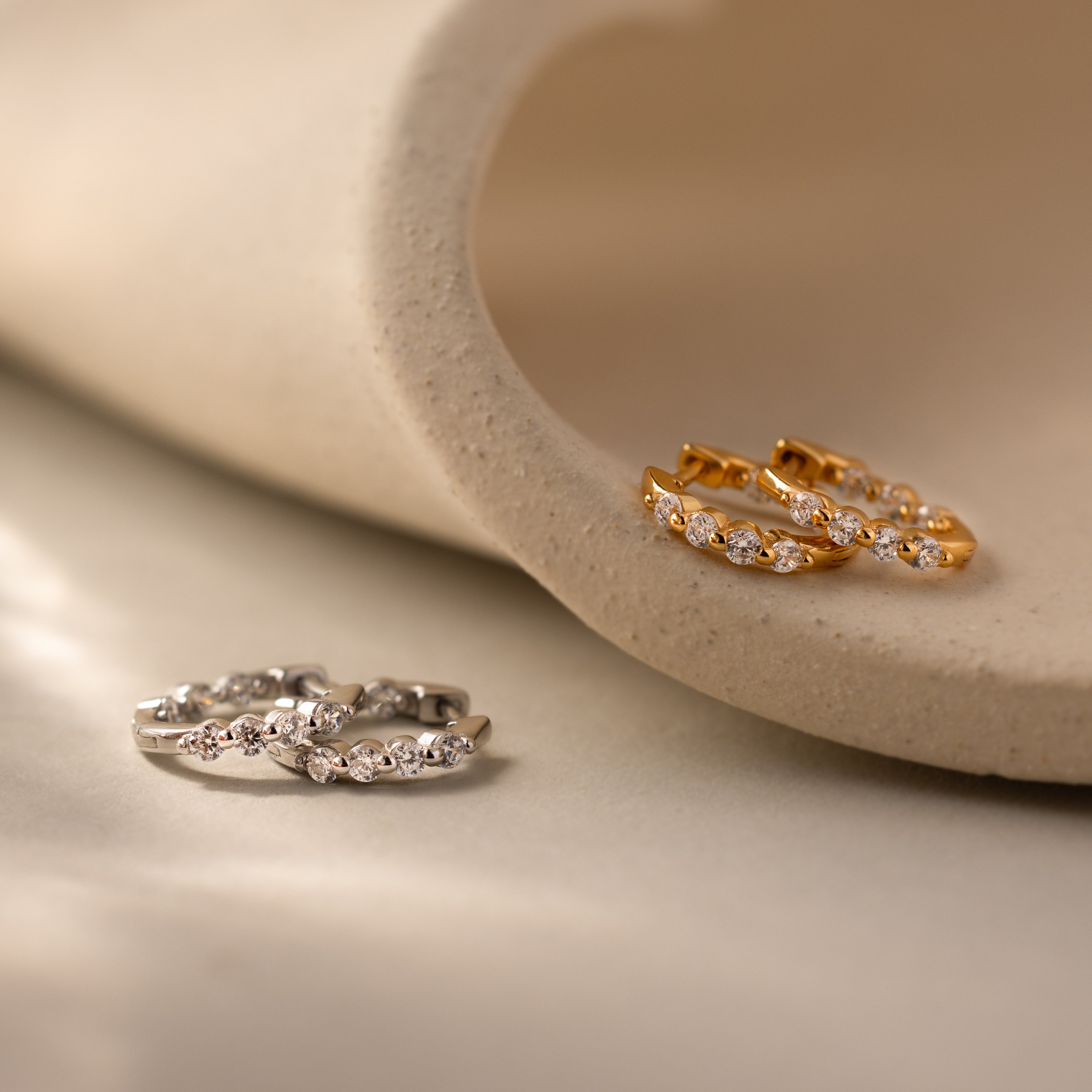 Mini Birthstone Beaded Huggies—gold and silver hoop earrings with gemstones—shown on a cream ceramic surface.