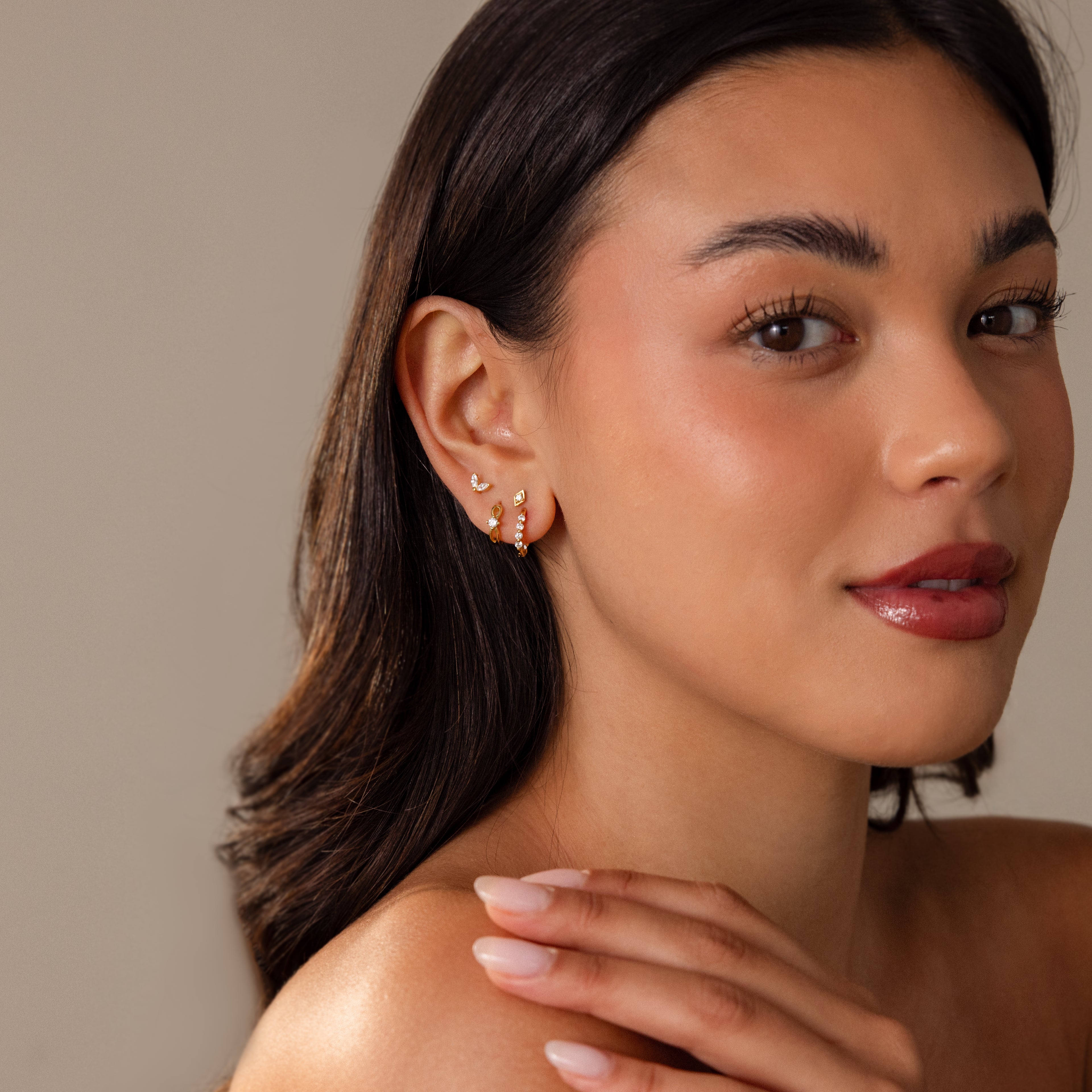 Woman with long dark hair, wearing Mini Birthstone Beaded Huggies and gold earrings, looks at the camera with a soft smile and natural makeup.