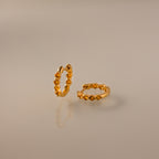 Mini Topaz Beaded Huggies featuring gold hoops with delicate beads, displayed on a smooth, reflective beige surface.