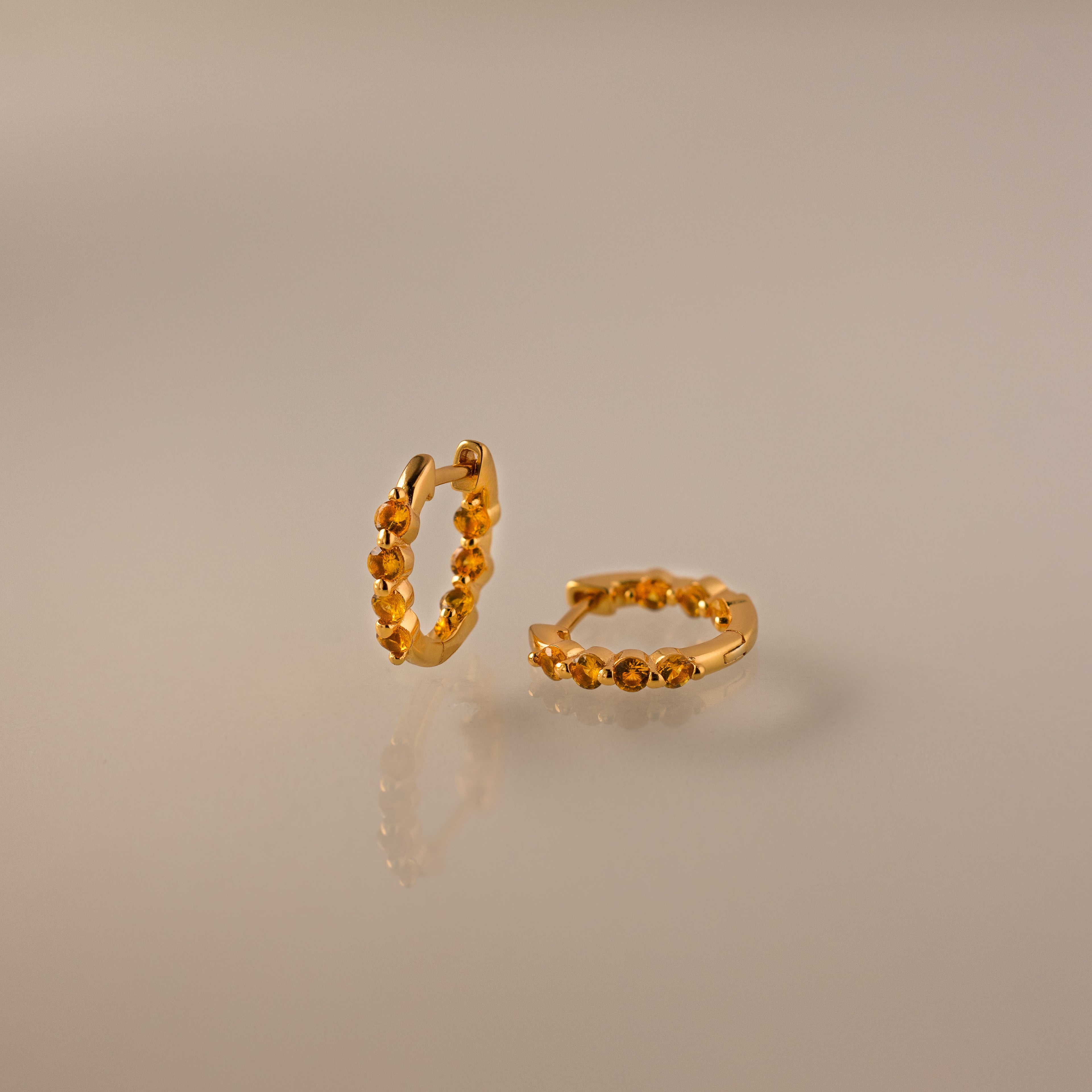 Mini Topaz Beaded Huggies featuring gold hoops with delicate beads, displayed on a smooth, reflective beige surface.