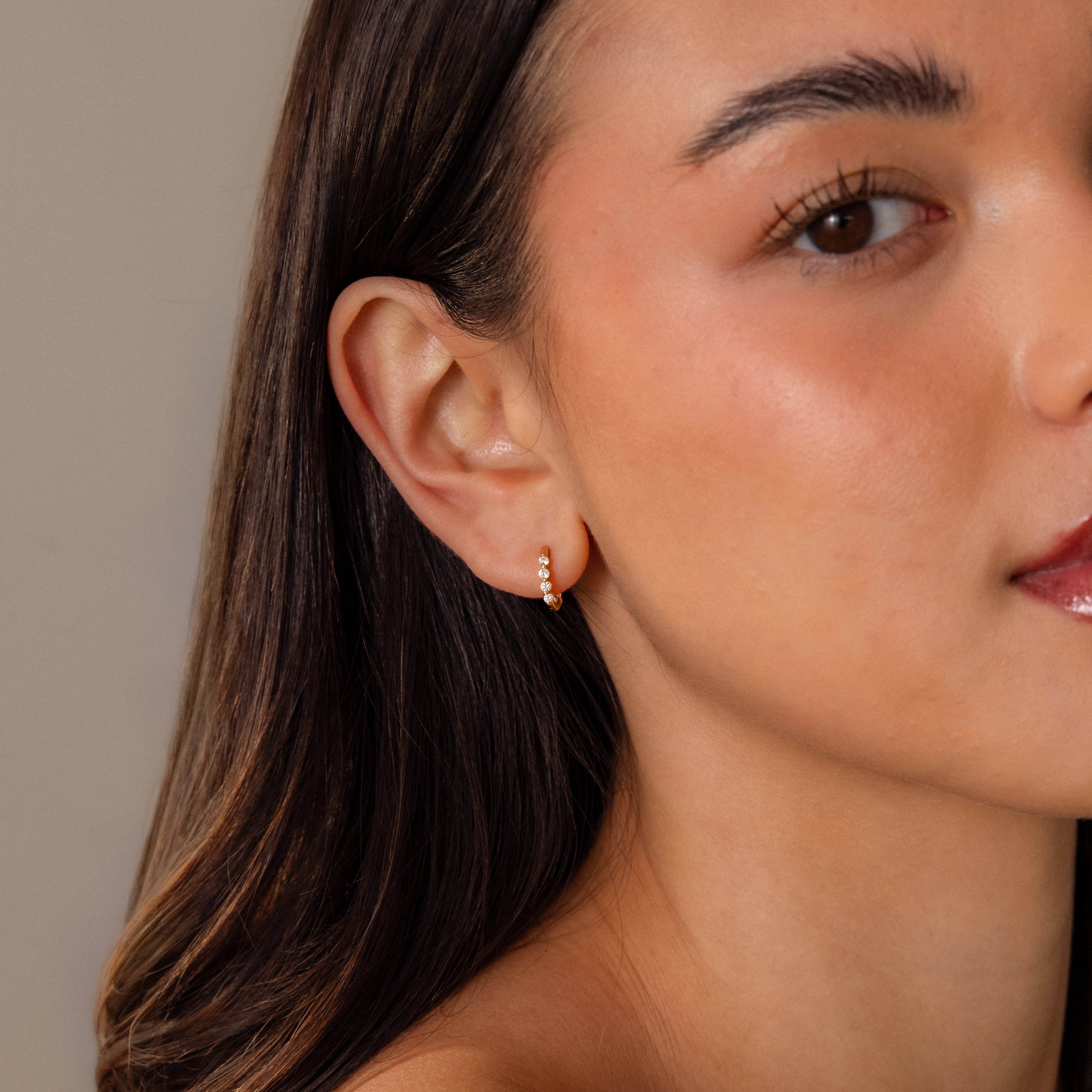 Woman with long dark hair wears Mini Topaz Beaded Huggies—modern small gold hoops with beaded details—shown from the side.