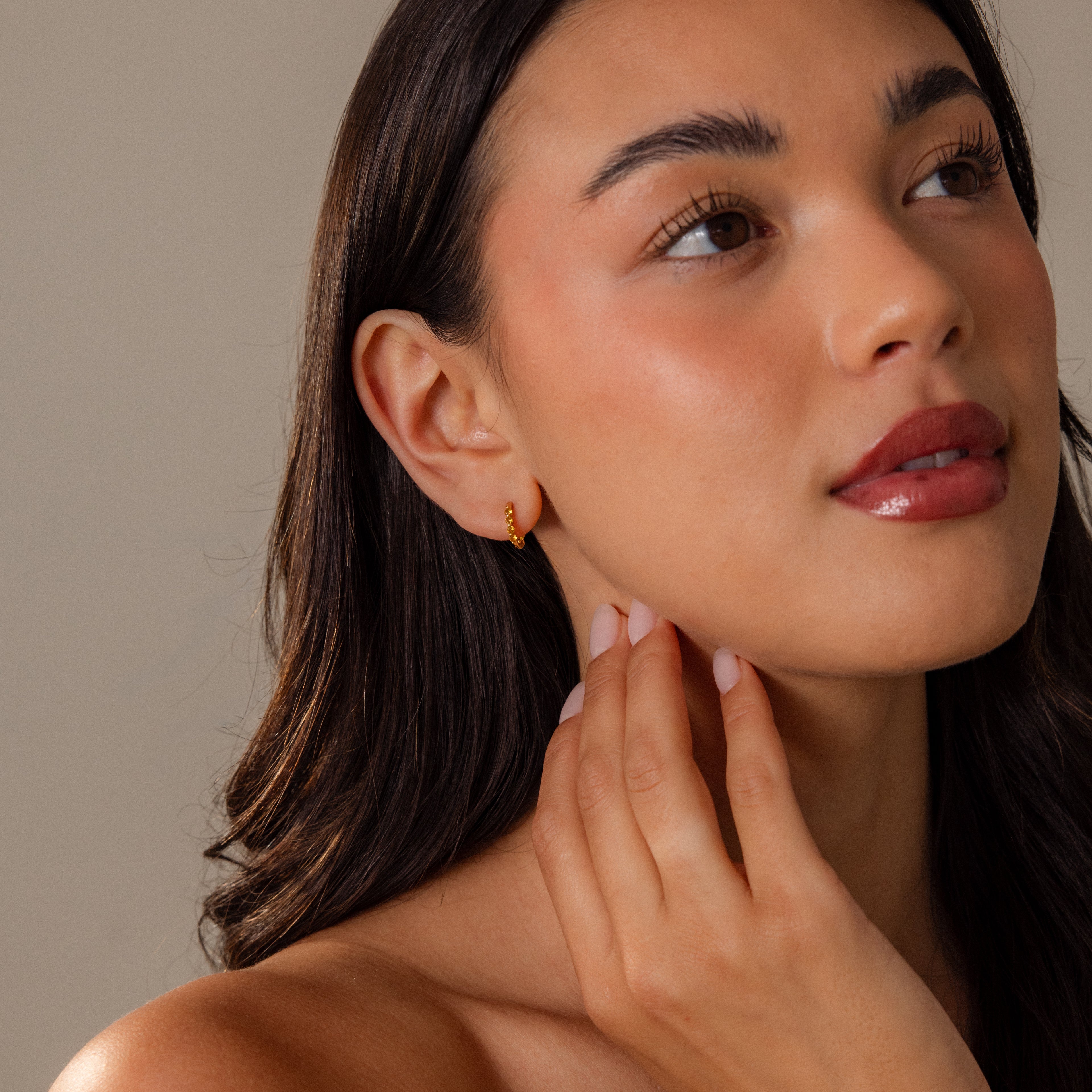 Woman with long dark hair touches her neck while looking upward, wearing Mini Topaz Beaded Huggies.