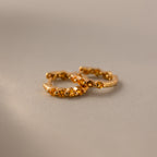Mini Topaz Beaded Huggies—gold huggie earrings with small decorative beads, shown on a neutral textured surface. Perfect as modern hoop earrings for any occasion.