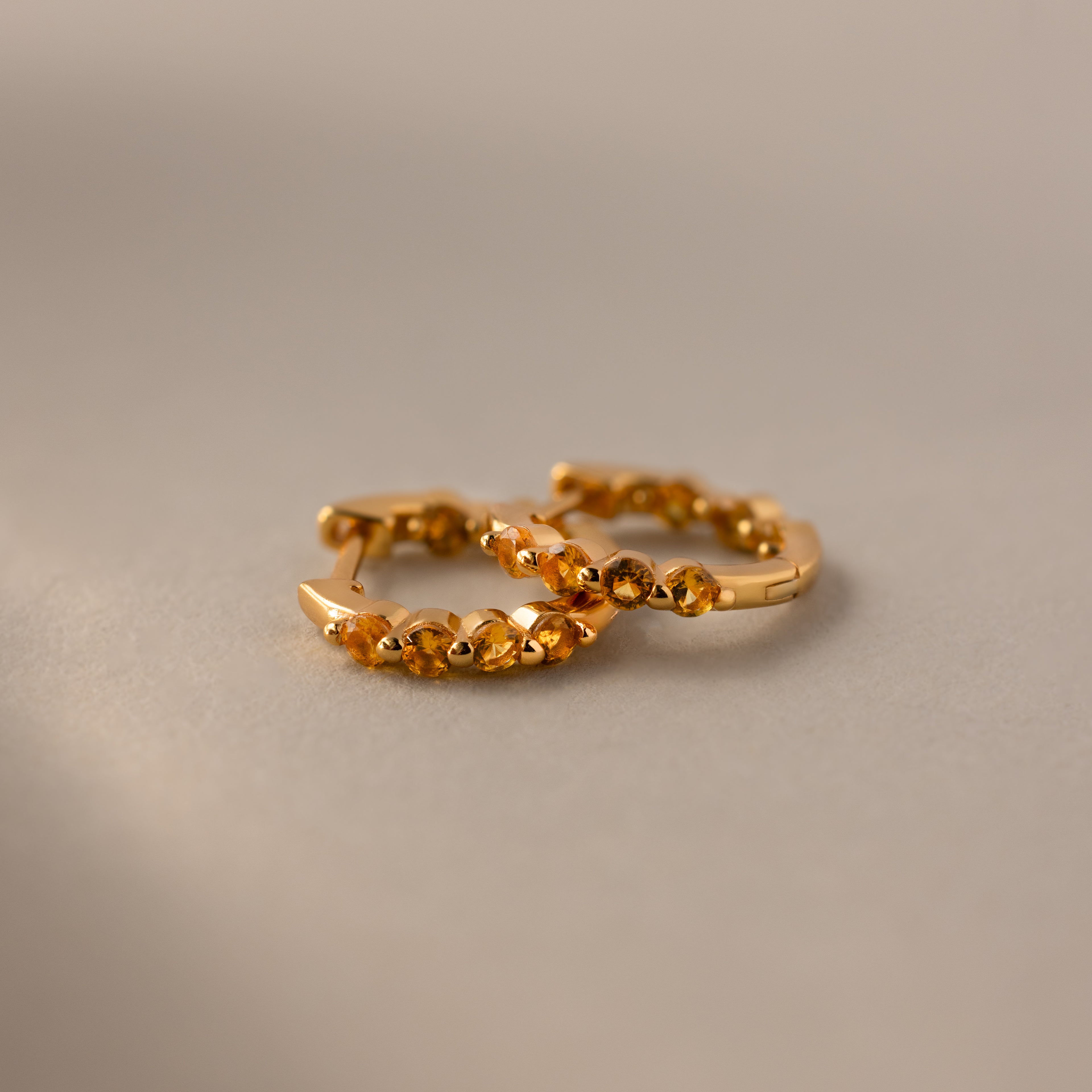 Mini Topaz Beaded Huggies—gold huggie earrings with small decorative beads, shown on a neutral textured surface. Perfect as modern hoop earrings for any occasion.