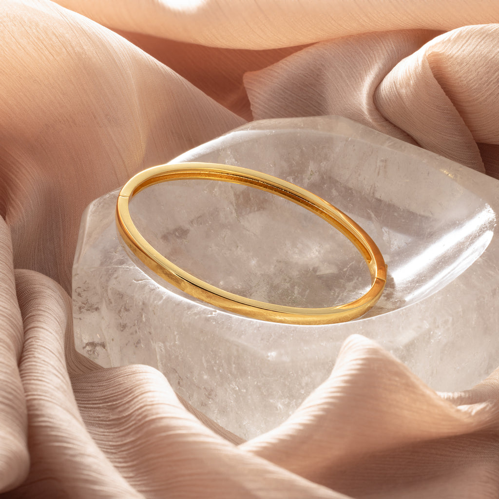 The Classic Bangle is showcased on a clear crystal and soft beige fabric, creating an elegant and chic jewelry display.