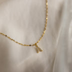 The Dainty Pave Letter Necklace in 18K Gold showcases a shimmering CZ diamond pavé letter A pendant on a gold mirror chain, elegantly displayed on soft, cream-colored fabric.