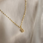 The Dainty Pave Letter Necklace in 18K Gold features a pavé letter B pendant with sparkling CZ diamonds, suspended on a gold mirror chain and elegantly displayed on soft, light-colored fabric.
