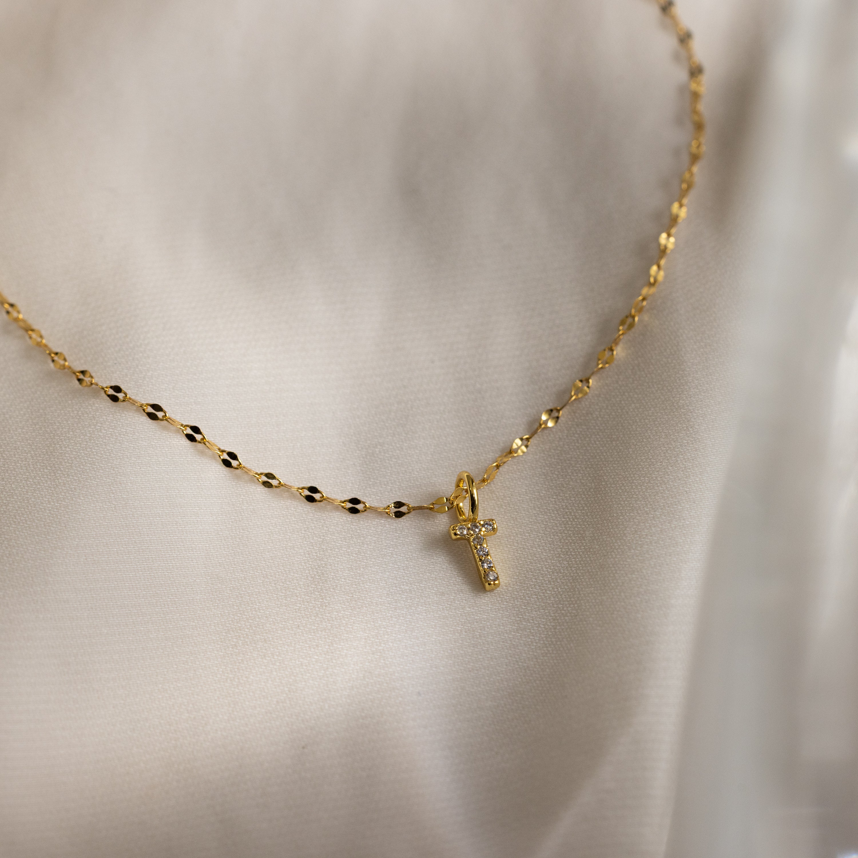 Dainty Pave Letter Necklace in 18K Gold shown on a cream fabric background.